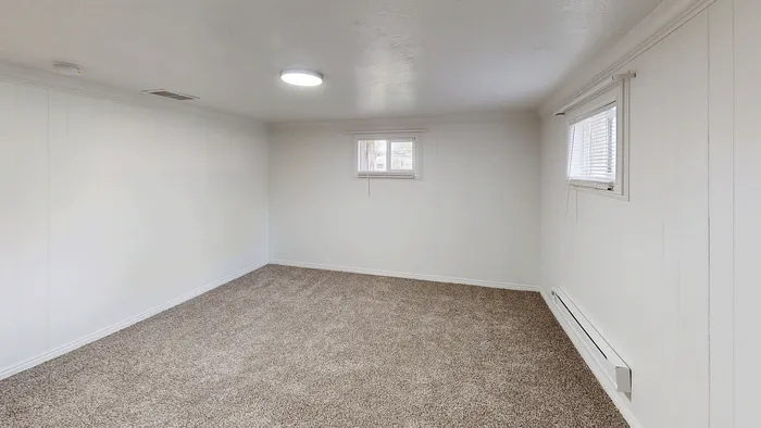 Basement bedroom with carpet flooring, natural light from two windows, and neutral paint at Woodside Creek Village.